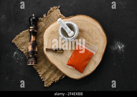 Sezione trasversale in legno con paprika affumicata in confezione di plastica e. mortaio di pietra e mulino Foto Stock