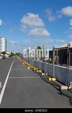 Una linea di recinzioni temporanee con basi gialle in cemento erette di fronte ad un sito di demolizione in una città regionale. Foto Stock