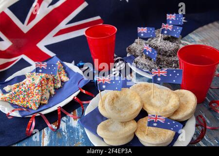 Cibo da festa tradizionalmente mangiato il 26 gennaio in Australia Day, con pane di fata, torte di carne e torte di lamington contro una bandiera australiana. Foto Stock