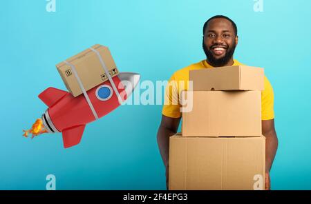 Happy boy riceve un pacchetto prioritario da online shop order. Concetto di corriere veloce come razzo. Sfondo blu. Foto Stock