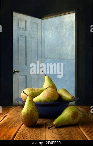 Sei pere da conferenza fresche disposte in un vetro blu chiaro ciotola posta su un tavolo di quercia planata e fotografata contro una porta bianca aperta Foto Stock