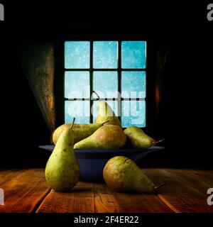 Sei pere da conferenza fresche disposte in un vetro blu chiaro ciotola posta su un tavolo di quercia planata e fotografata contro una finestra Foto Stock