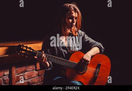 Donna che suona la chitarra, tenendo una chitarra acustica tra le mani. Ragazza suona la chitarra. Donna hipster uomo seduto in un pub Foto Stock