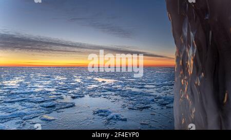 Paesaggio invernale in spiaggia, costa con ghiaccio crepato, neve e acqua di mare aperta al tramonto. Foto Stock
