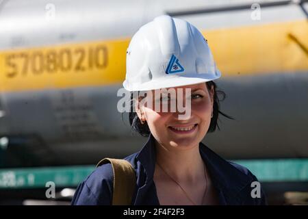 Impianto chimico caustico. Attraente giovane ingegnere ragazza in hardHat bianco che posa e sorridente sullo sfondo del carro armato ferroviario. Foto Stock