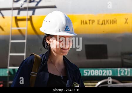 Impianto chimico caustico. Giovane attraente ingegnere ragazza in bianco hardHat che posa e sorridendo sul carro ferroviario carro armato backgd. Foto Stock