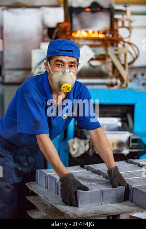 Taldykorgan, Kazakhstan - Giugno 06 2012: Impianto di riciclaggio degli accumulatori Kainar. Giovane lavoratore asiatico in respiratore smistamento piombo piastre batteria. Foto Stock