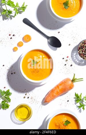 Flay Lay, tre ciotole per zuppa di carote e una carota su sfondo bianco. Vista dall'alto. Formato verticale. Foto Stock