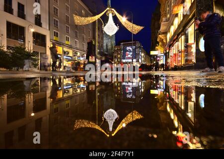 Vienna Graben Street nel periodo natalizio si riflette in una pozza d'acqua, mentre i turisti sono visite turistiche e shopping. Foto Stock