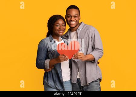 Gioiosa coppia nera amorevole che tiene insieme il cuore di carta rossa e. Agguato Foto Stock