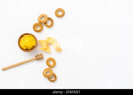 miele in una ciotola di legno, bagel e formaggio su sfondo bianco Foto Stock