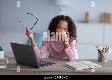 Stanco nero studentessa strofinare occhi irritati asciutti, studiando online sul computer portatile a casa Foto Stock