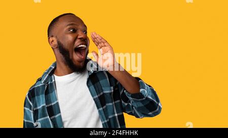 Black Guy gridando tenere la mano vicino alla bocca su sfondo giallo Foto Stock