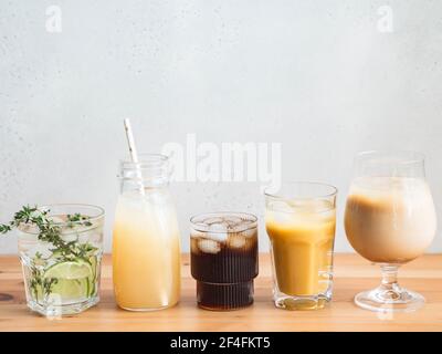 Varie bevande analcoliche rinfrescanti in bicchieri con ghiaccio. Succo di frutta, limonate, caffè ghiacciato, frullati su tavolo di legno. Spazio di copia. Vista frontale Foto Stock