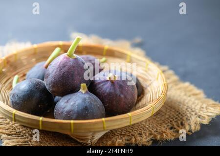 Fichi maturi freschi in cesto di bambù su tavolo scuro. Sano frutto di fico mediterraneo. Fichi freschi su sfondo nero. Foto Stock