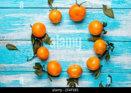 Tangerini con foglie verdi sul frutto e sul tavolo, adagiati in cerchio su un tavolo di legno blu. La vista dall'alto. Spazio di copia. Foto Stock