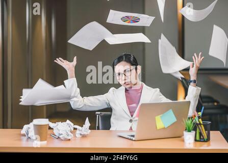 Donna d'affari asiatica arrabbiata gettando carte su se stessa in ufficio quando il lavoro fallisce, progetto fallito, lavoro duro e overworked e ha sottolineato Concep Foto Stock