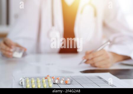 Donna-medico sconosciuto riempie in su la forma di prescrizione in stanza soleggiata, primo piano Foto Stock