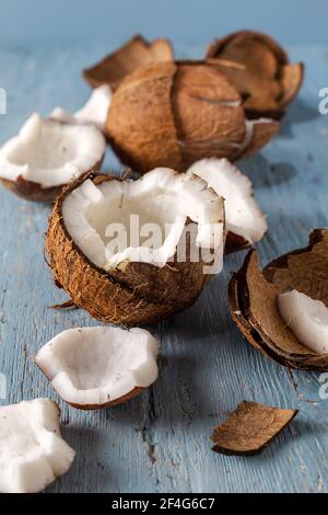 Le metà e i pezzi di cocco con un bicchiere di latte di cocco su uno sfondo di legno naturale blu. Foto Stock