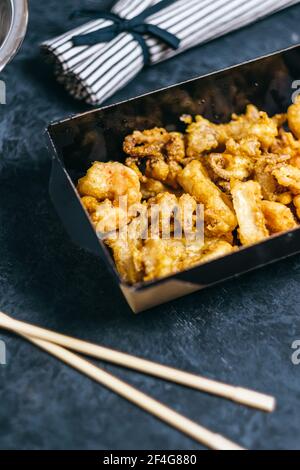 Gamberetti, calamari e polpi cotti in pastella in una scatola nera di carta su sfondo scuro. Foto Stock