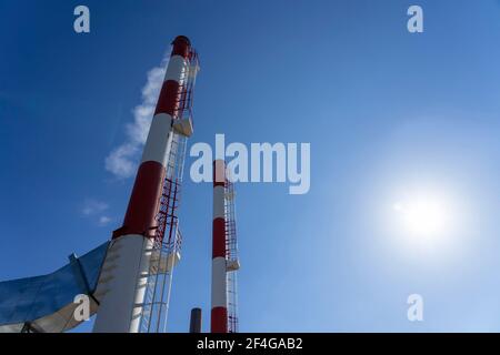 Fumo proveniente dalla centrale industriale Chimneys. Esterno dell'impianto di riscaldamento urbano con camini industriali contro il sole e il cielo blu. Foto Stock