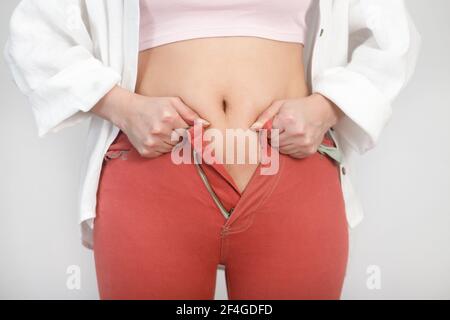 Primo piano di stomaco donna grasso non può fissare una zip su jeans. Dieta, peso, concetto di obesità. Foto Stock