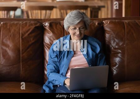 Anziana signora latina sedersi sul divano tenere il computer portatile sulle ginocchia Foto Stock