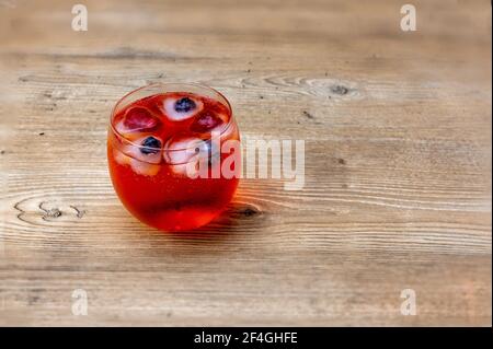 cocktail di bibite rosse e vodka con lampone e mirtillo a forma di cuore ghiaccio su tavolo di legno Foto Stock