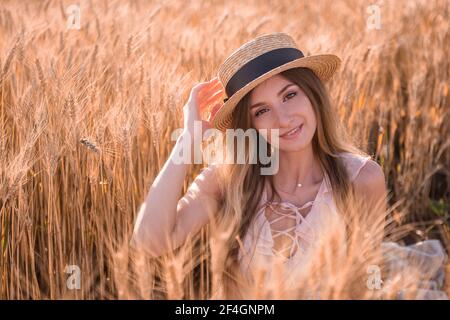 Giovane donna bionda in cappello di paglia sullo sfondo di un campo di dorati spikelets di grano, segale. Primo piano ritratto di bella ragazza con occhi marroni. W Foto Stock