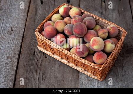 Pesche fresche frutta in cestino su sfondo rustico di legno scuro, vista dall'alto. Raccolta estiva di frutta. Vita morta. Un gruppo di pesche mature. Piatto posare vegan Foto Stock
