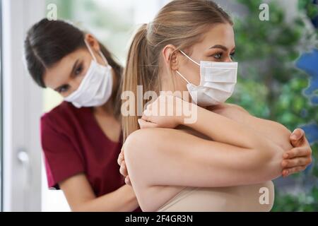 Fisioterapista in maschera che aiuta la paziente femminile Foto Stock