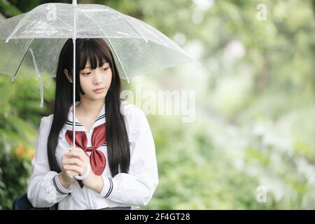 Ritratto di scuola asiatica ragazza camminare con ombrellone in natura la passerella a piovere Foto Stock