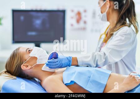 Medico in maschera controllo tiroide alla sua paziente femminile Foto Stock