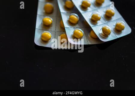Compresse gialle in blister su sfondo nero Foto Stock