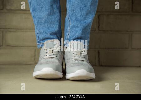 Una donna in sneakers bianco si trova contro un muro di mattoni sullo sfondo. Piedi in scarpe sportive senza marchio Foto Stock