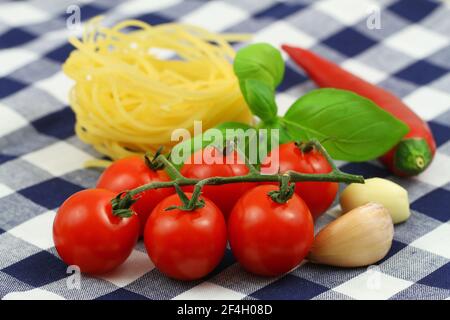 Pasta ingredienti: Tagliatelle non cotte, pomodori ciliegini su gambo, foglie di basilico fresco e peperoncino rosso Foto Stock