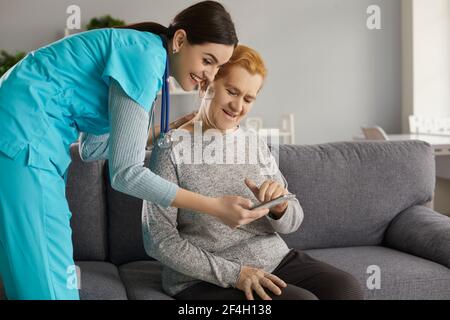 Infermiere che insegna a una donna anziana a utilizzare l'app di monitoraggio della salute su tablet o telefono cellulare Foto Stock