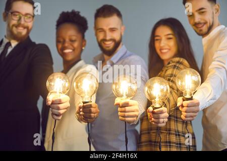 Gruppo di giovani creativi felici uomini d'affari diversi che tengono luminoso lampadine Foto Stock