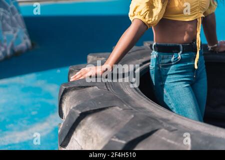 Mano di una ragazza afroamericana in una t-shirt gialla sulla ruota di un trattore. Sfondo blu. Foto Stock