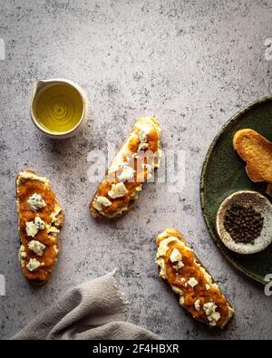 Disposizione superiore di pane di zucca sano toast con marmellata dolce e formaggio di capra messo su tavola di marmo vicino a caraffa di olio d'oliva Foto Stock