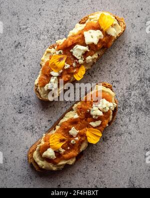 Vista dall'alto dei toast di pan di zucca appena sfornati con marmellata dolce e formaggio di capra decorato con petali di fiori gialli e servita su tavola di marmo Foto Stock