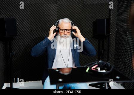 Anziano ha sopportato il maschio nelle cuffie seduto in stanza insonorizzata durante esame audiologico e test uditivo Foto Stock