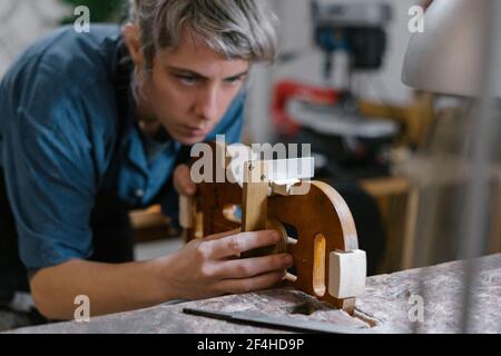 Donna artigiana in grembiule che prende i passi nella fabbricazione del violino in studio professionale Foto Stock