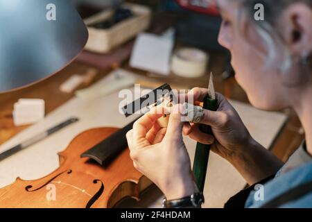 Dall'alto femmina artigianale taglio decorazione in legno per violino fatto a mano durante il lavoro in officina Foto Stock