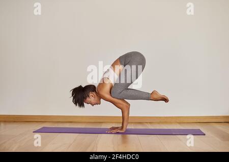 Vista laterale di una donna robusta in abbigliamento sportivo in piedi a Bakasana posa al piano in studio Foto Stock