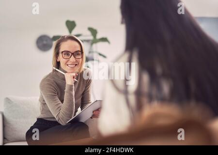 Allegro consulente femminile ascoltando cliente anonimo mentre aiuta durante sessione di terapia mentale Foto Stock