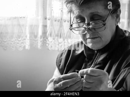 Foto in bianco e nero di una donna anziana che si sta infilando a. ago Foto Stock