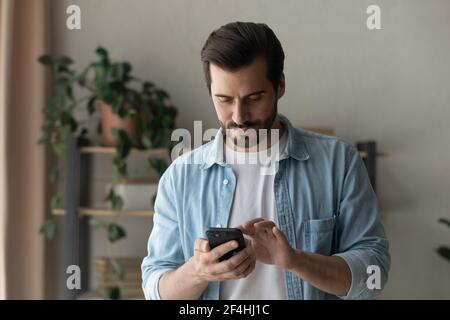 Primo piano uomo concentrato guardando lo schermo del telefono, in piedi Foto Stock