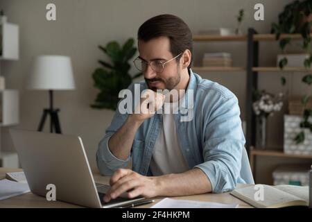 Primo piano uomo attento che indossa occhiali guardando lo schermo del computer portatile Foto Stock