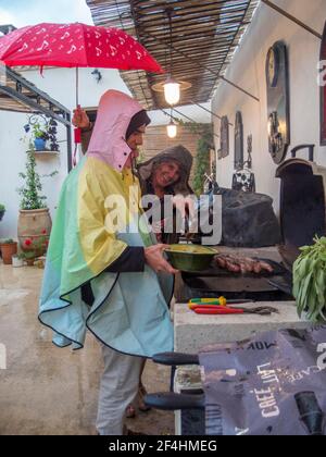 Barbecue in coppia nel patio in tempo umido, al riparo sotto un ombrello rosso. Uzès, Gard, Languedoc, Francia meridionale. Foto Stock